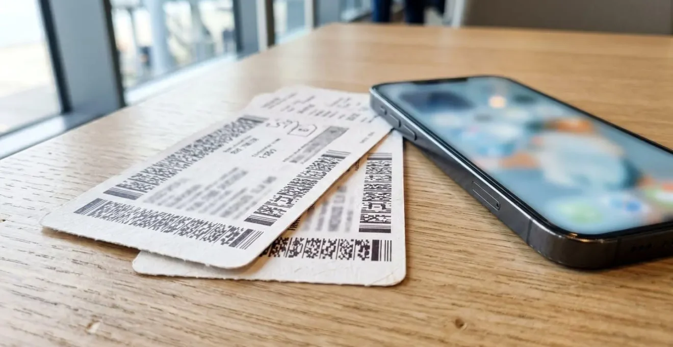 Extreme Nahaufnahme von Fährtickets auf sauberem Tisch, Smartphone daneben mit unscharfem Bildschirm, moderne Oberfläche bei natürlichem Seitenlicht